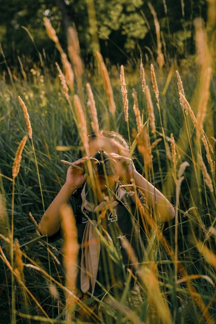 A young child uses binoculars to explore nature in a grassy field during the summer.